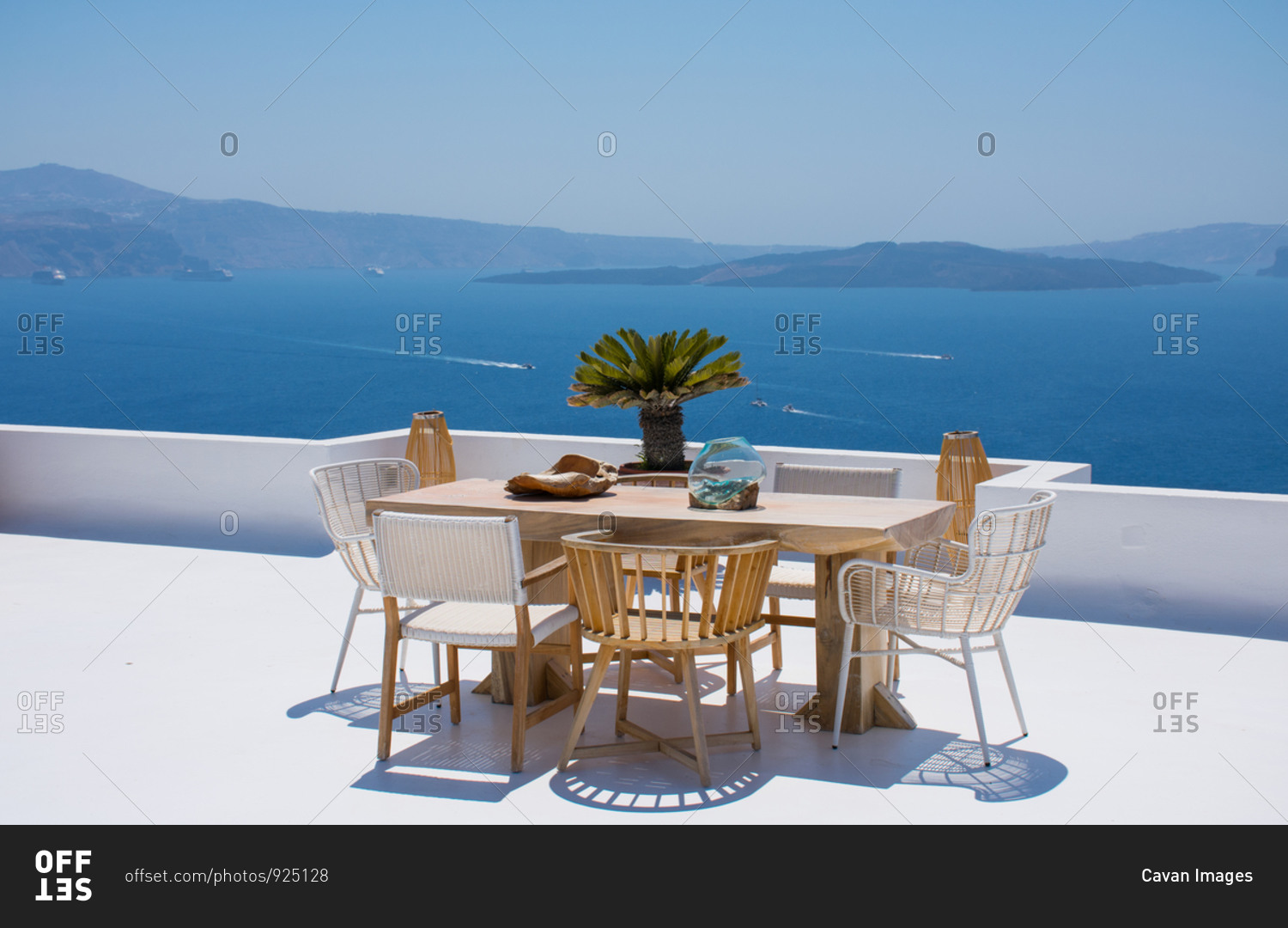 furniture composed by a table and some chairs on a white terrace of a house in Santorini Greece where you can enjoy meal while seeing a romantic seascape to the blue Aegean sea. Horizontal ph