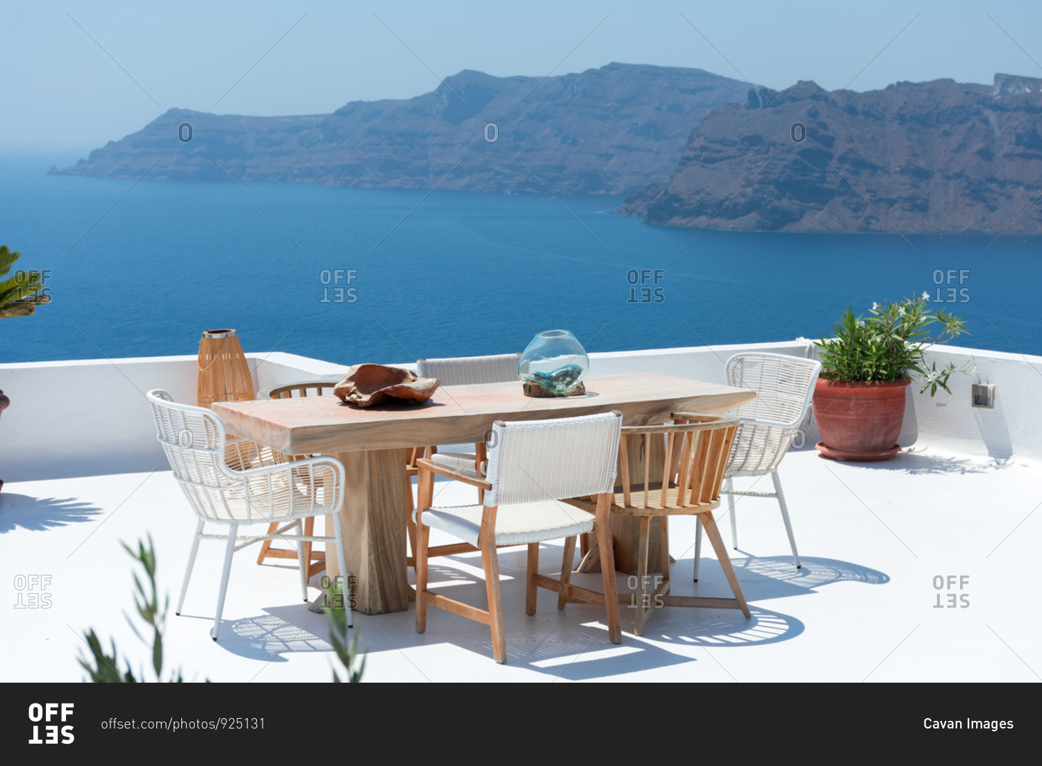 furniture composed by a table and some chairs on a white terrace of a house in Santorini Greece where you can enjoy meal while seeing a romantic seascape to the blue Aegean sea. Horizontal ph