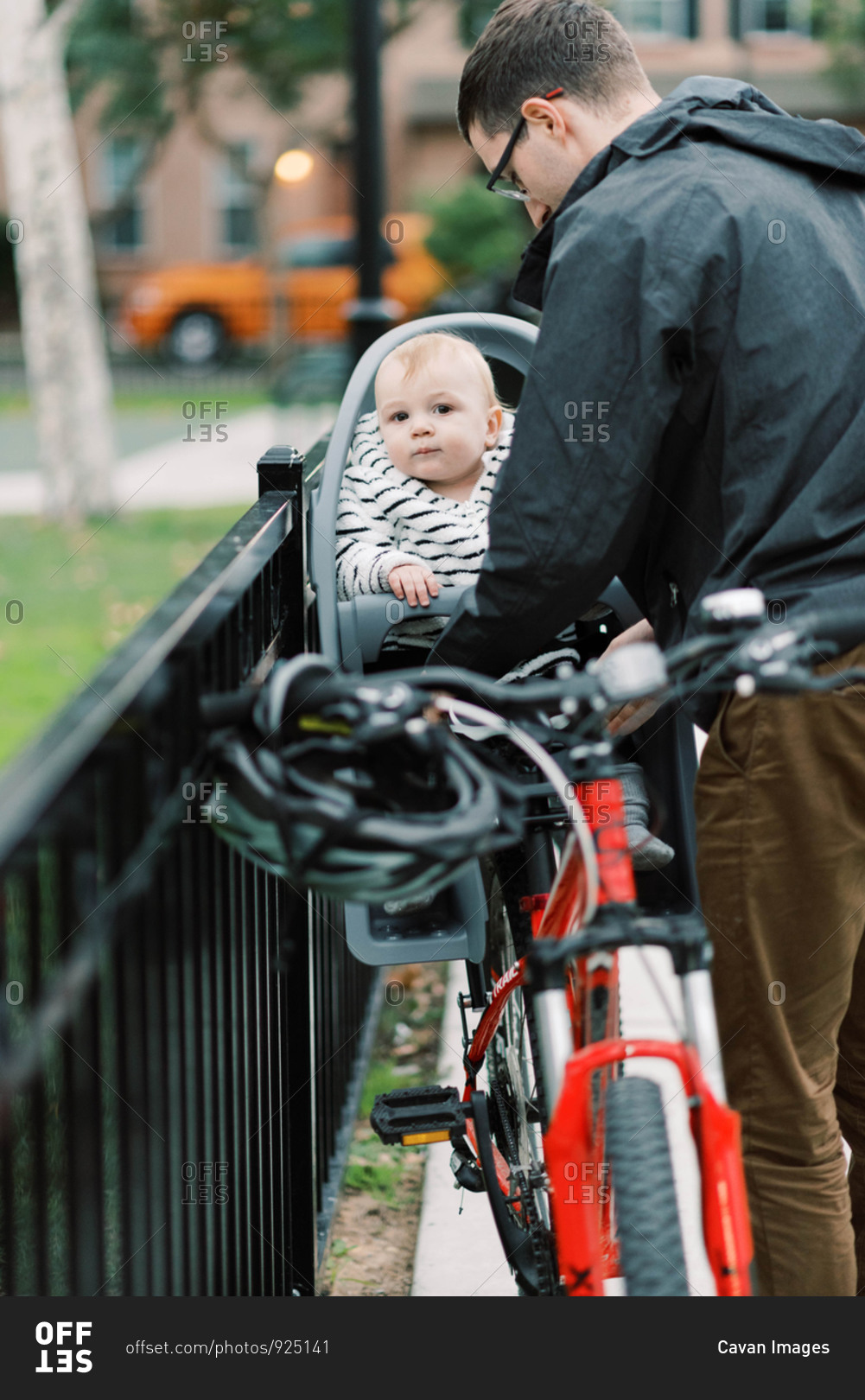 A young millennial dad strapping his son in his bike seat.