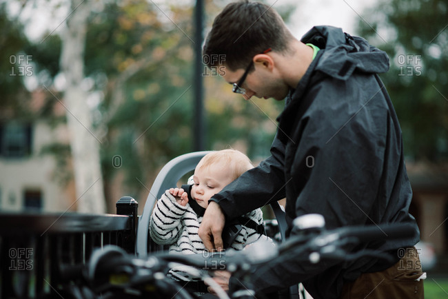 A young millennial dad strapping his son in his bike seat.