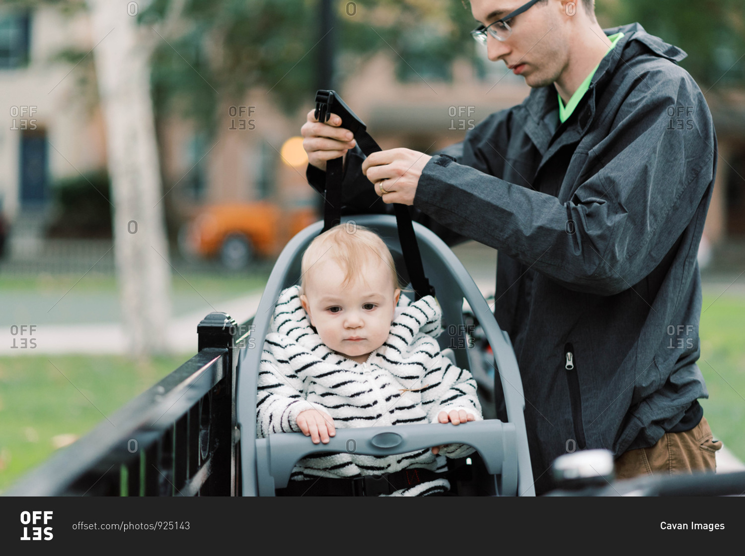 A young millennial dad strapping his son in his bike seat.