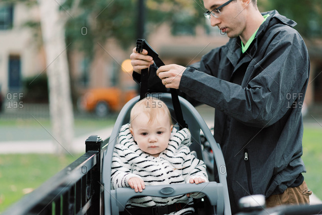 A young millennial dad strapping his son in his bike seat.