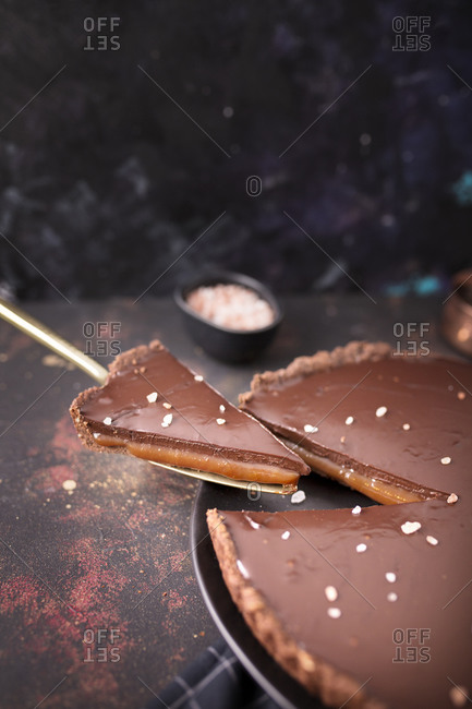 Serving a slice of a salted caramel and chocolate tart on dark background