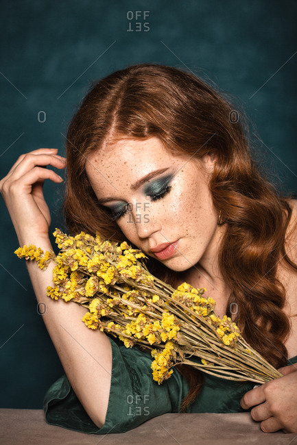 Melancholic beutiful ginger girl with a yellow flowers posing in studio