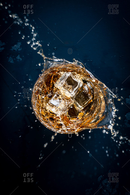 Ice splashing into a glass of bourbon on dark blue background