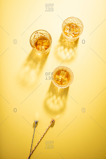 Glasses of bourbon on bright yellow background with stir sticks