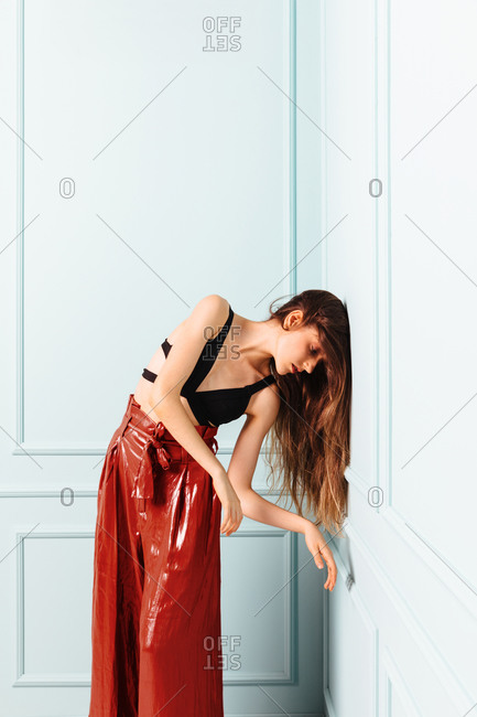 Young girl leaning her head against the wall in a defeated attitude. Fashion girl with red pants on turquoise background.