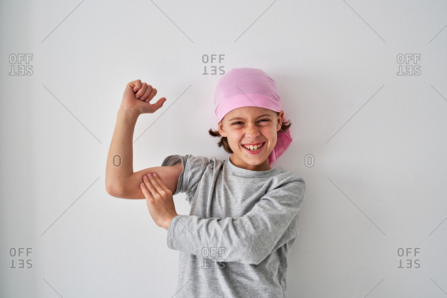 Brave small child with cancer diagnosis looking at camera and screaming while raising fists up on gray background
