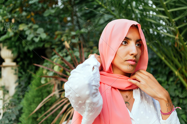 Portrait of a beautiful young Muslim woman putting on hijab in a garden