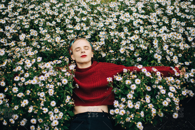Contemplating man wearing red lipstick sleeping amidst daisy flowering plants