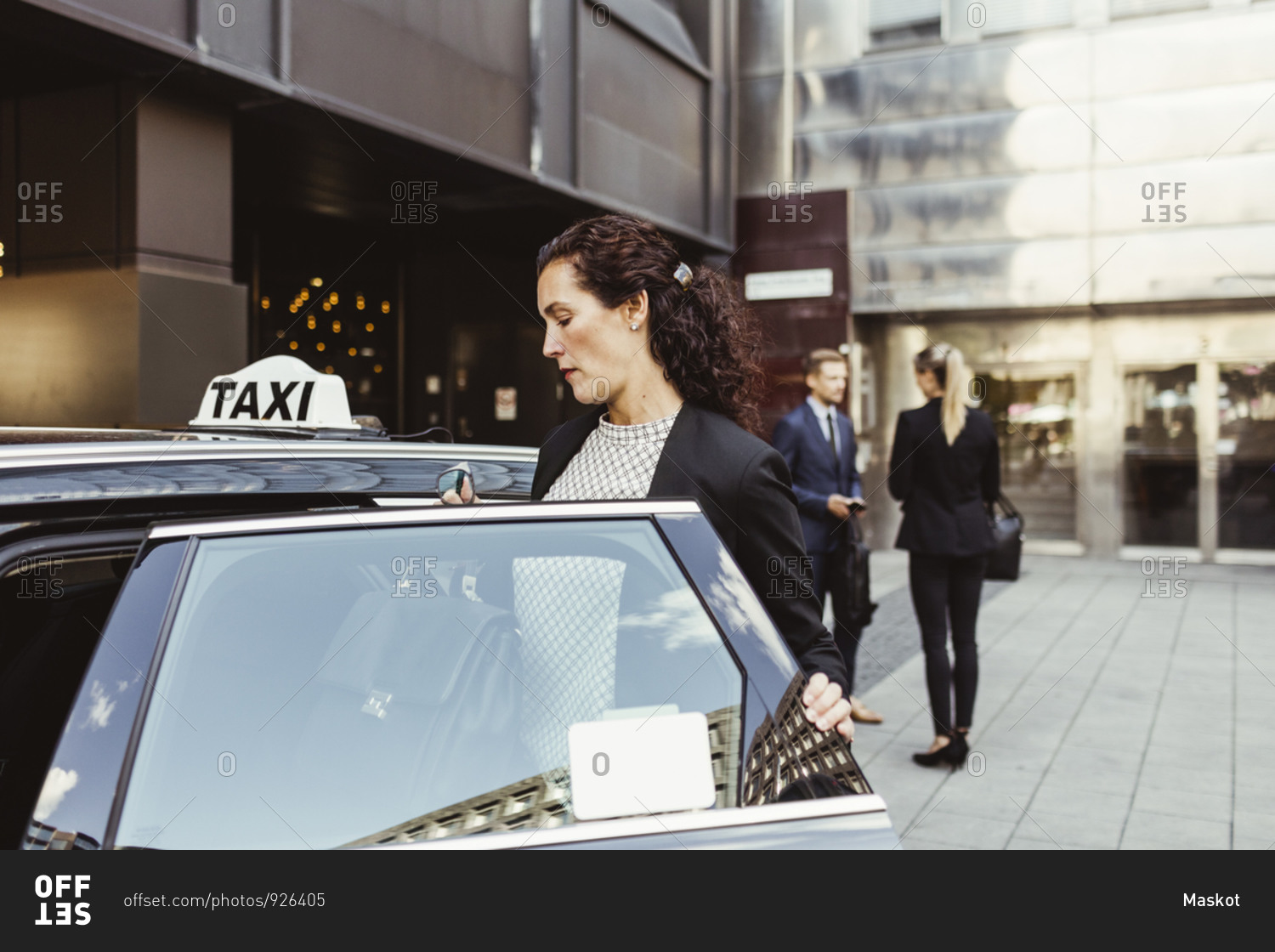 Female entrepreneur entering in taxi while coworkers standing in background
