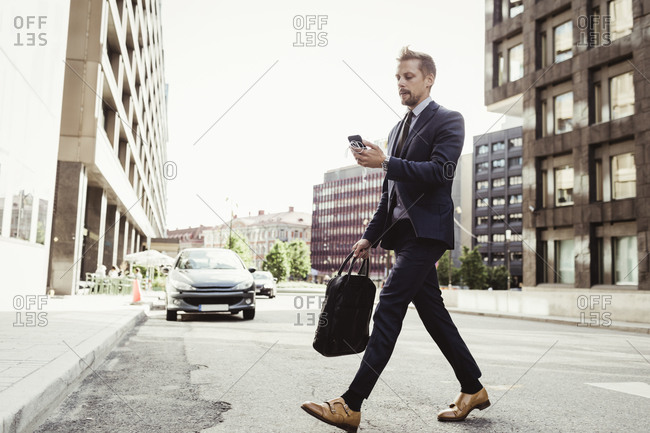 Male entrepreneur looking at phone while crossing street