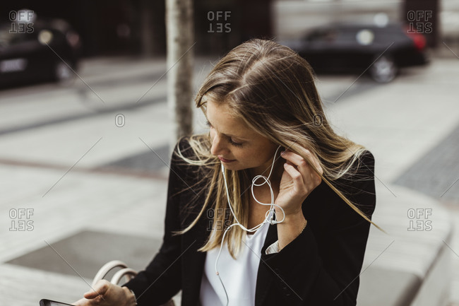 Businesswoman with in-ear headphones sitting outdoors