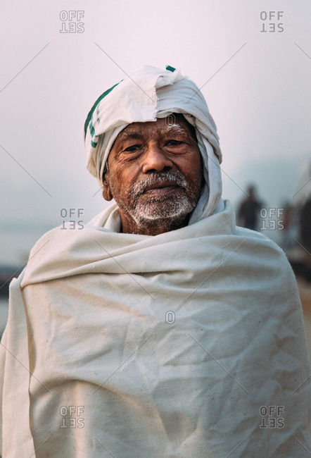 Varanasi, India - FEBRUARY, 2018: Close-up portrait of Elderly Indian man wearing traditional white clothes standing on river bank