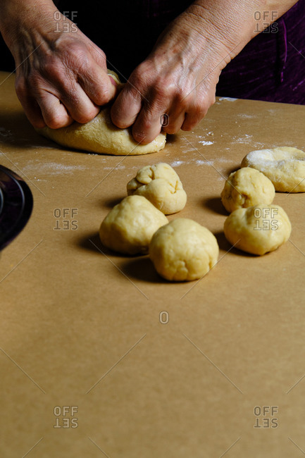 Unrecognizable lady rolling small balls from soft dough while cooking pastry on table in kitchen