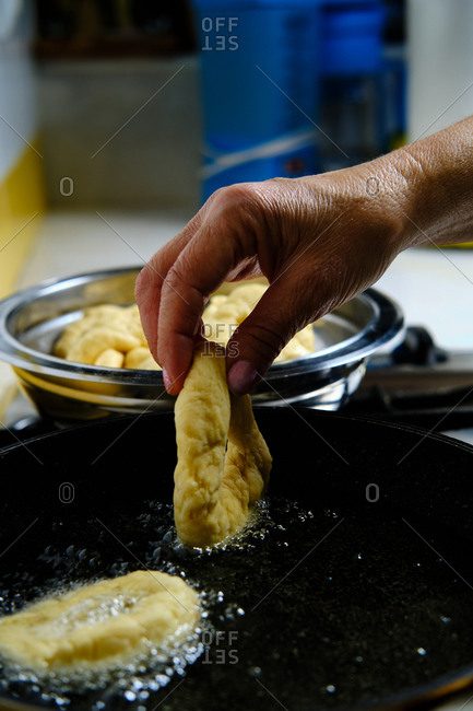 From above unrecognizable person hands with bunch of delicious doughnuts frying in hot bubbling oil on stove in kitchen