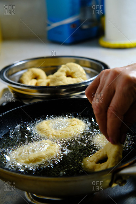 From above unrecognizable person hands with bunch of delicious doughnuts frying in hot bubbling oil on stove in kitchen