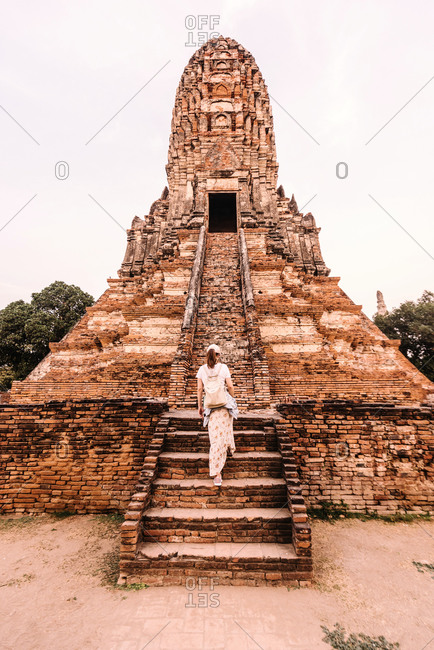 Back view of female traveler in casual clothes climbing on ancient stairs of big oriental old temple in Thailand
