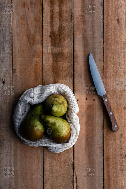 Top view of cotton sack with juicy fresh pears placed on wooden table with knife