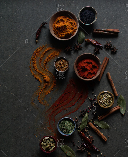 Top view composition with different kinds of natural aromatic spices placed on dark gray background with powder spice spilled on the surface