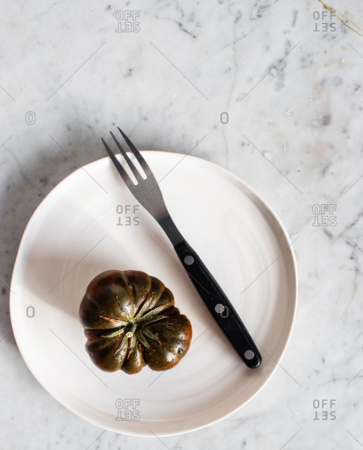 Top view of big unripe green tomatoes on black plate with metal fork and piece of cheese on plate