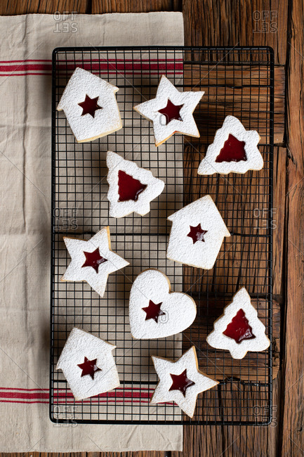 Top view of tasty homemade cookies of various shapes with red berry jam and white sugar powder placed on wooden table with utensils and decorative elements for Christmas celebration
