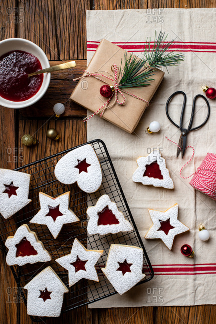 Top view of tasty homemade cookies of various shapes with red berry jam and white sugar powder placed on wooden table with utensils and decorative elements for Christmas celebration