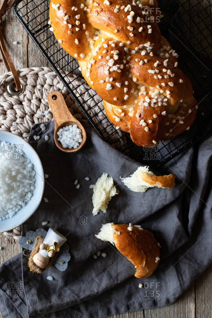 Top view of fresh appetizing braided round bread with sprinkles placed on metal grid on table with Christmas decorative elements