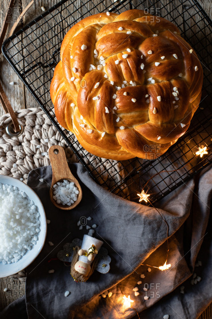 Top view of fresh appetizing braided round bread with sprinkles placed on metal grid on table with Christmas decorative elements
