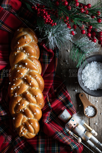 Top view of wooden table with cut traditional braided bread and knife placed on checkered Christmas tablecloth with decorative objects