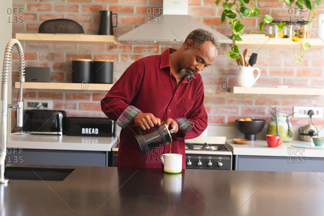 Senior retired African American man at home standing in the kitchen, carefully pouring a mug of coffee from a cafetiere, at home isolating during coronavirus covid19 pandemic