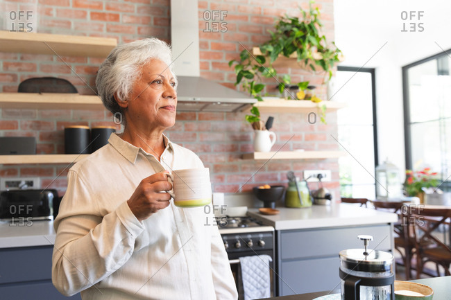 Senior retired African American woman at home standing in the kitchen, holding a mug of coffee and looking away, at home isolating during coronavirus covid19 pandemic