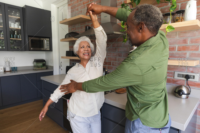 Happy senior retired African American couple at home holding hands, dancing together and smiling in their kitchen, at home together isolating during coronavirus covid19 pandemic