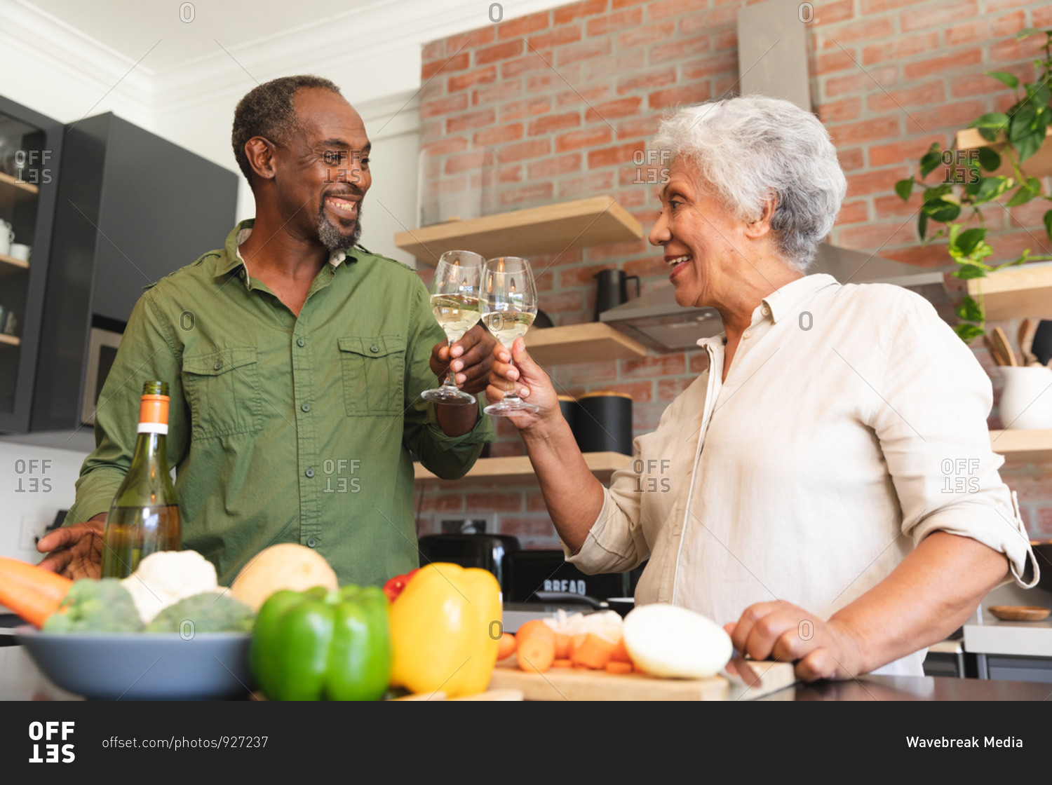 Happy senior retired African American couple at home, preparing vegetables to make a meal, and making a toast with glasses of white wine, couple at home together isolating during coronavirus covid19 pandemic
