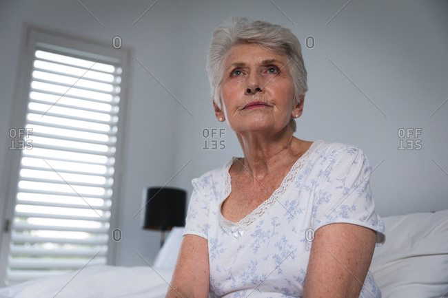 Close up of a retired senior Caucasian woman at home sitting up in bed in her nightclothes and looking away, self isolating during coronavirus covid19 pandemic