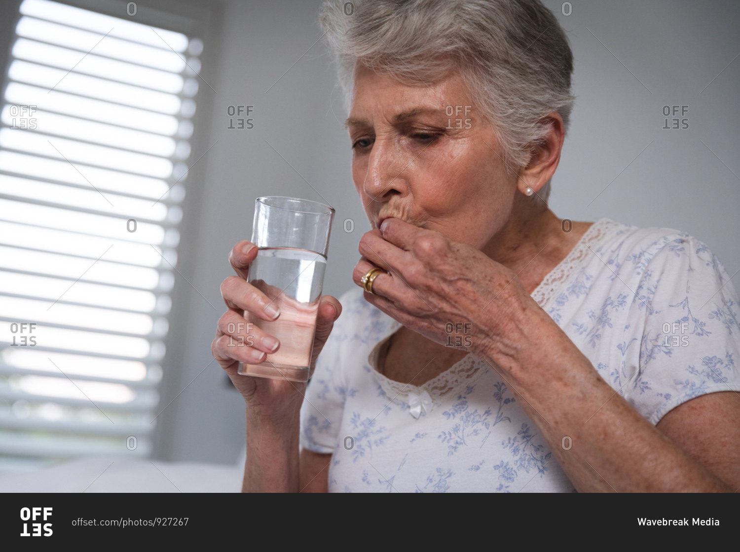 Close up of a retired senior Caucasian woman at home sitting up in bed in her bedroom holding a glass of water and taking medication, self isolating during coronavirus covid19 pandemic