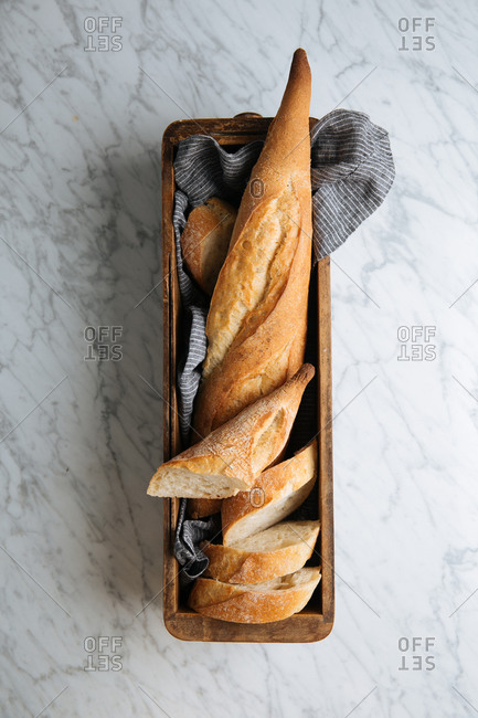Top view of delicious fresh sliced baguette served on wooden tray placed on marble table