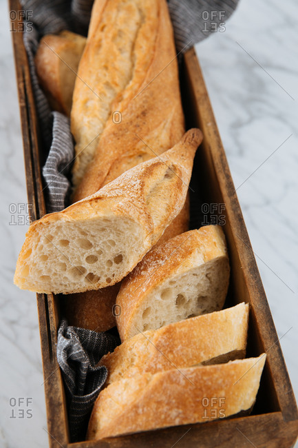 Top view of delicious fresh sliced baguette served on wooden tray placed on marble table