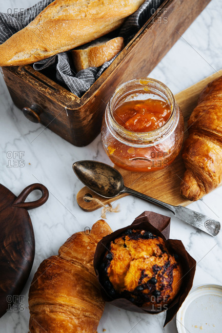 Top view composition of fresh baguette and croissants served with aromatic sweet apricot jam on marble table