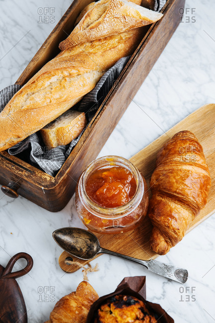 Top view composition of fresh baguette and croissants served with aromatic sweet apricot jam on marble table