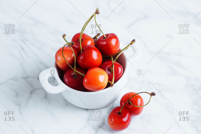 Fresh ripe red cherry with stalks in white ceramic pot placed on marble table against white wall