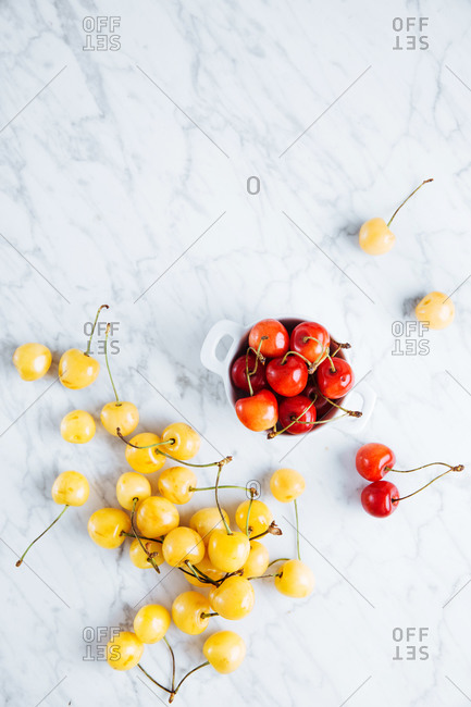 Top view of pot with fresh ripe red yellow cherries placed near fallen glass with yellow cherries on marble table