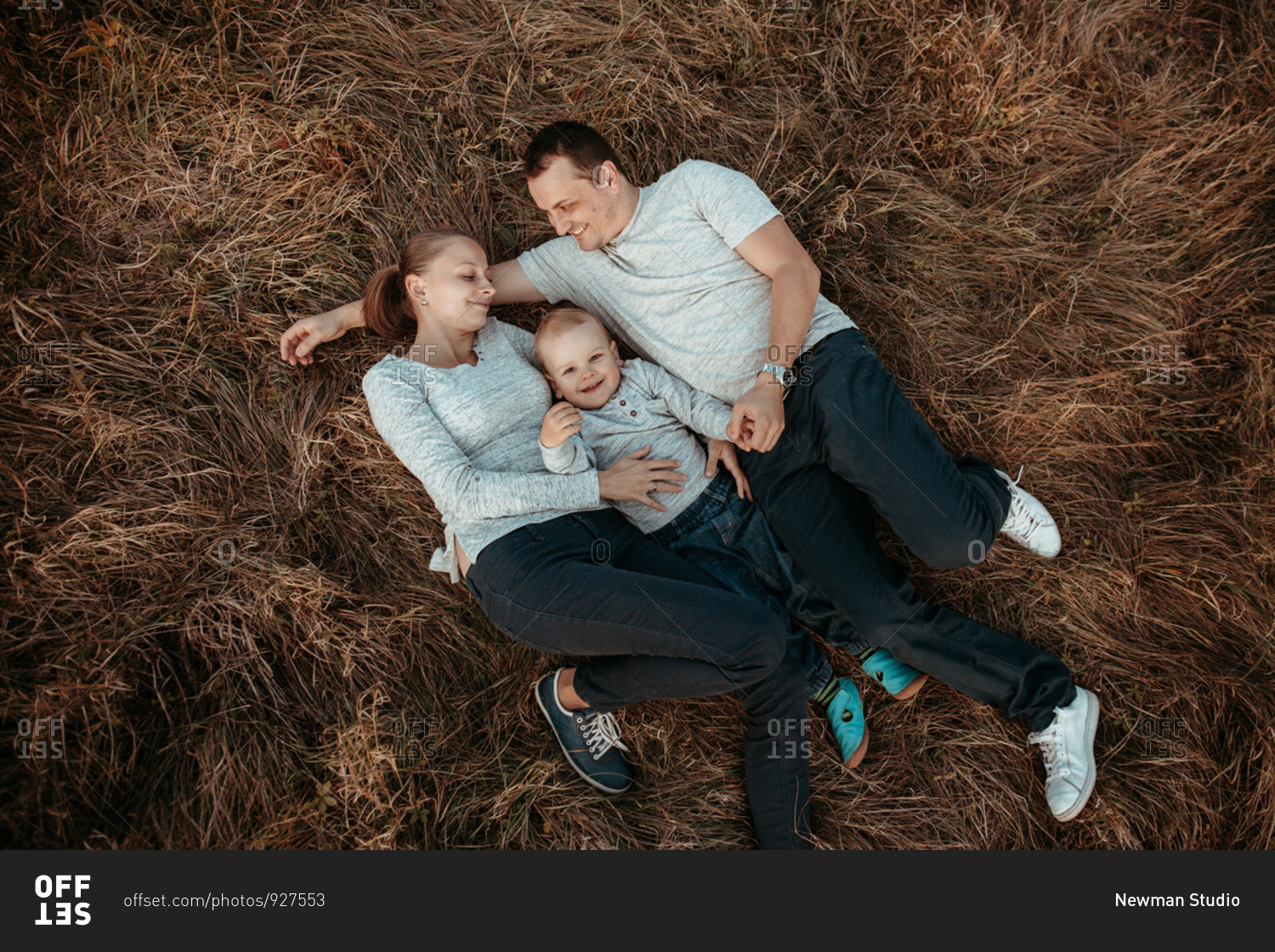 Parents with young son lying in filed high angle. Mother and father in field with son looking at camera and smiling.