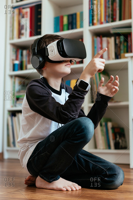 Teenage boy sitting on the floor wearing VR headset. Boy wearing VR glasses with headphones and interacting.