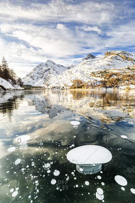 Methane bubbles in the icy surface of Silsersee with snowy peak, Lake Sils, Engadine Valley, Graubunden, Swiss Alps, Switzerland, Europe