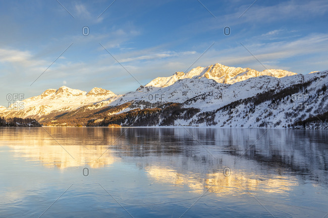 Mountains illuminated by sun at sunset reflected on the icy surfaces of Lake Sils, Engadine, Graubunden, Switzerland, Europe