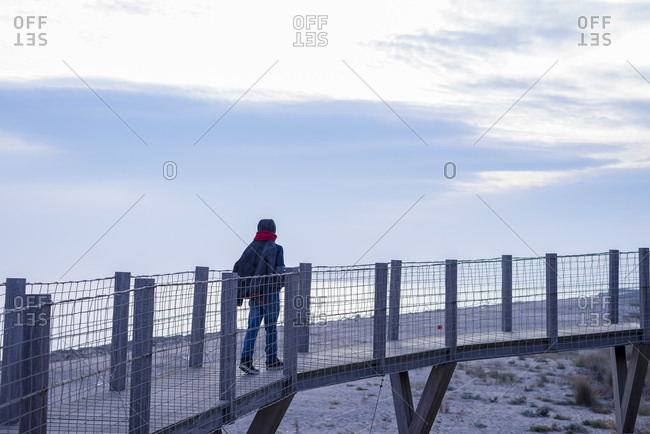 Young teen walking over a wooden gangplank near the sea at sunset