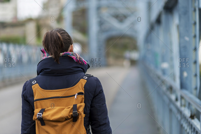 Front view of a ponytail woman with backpack walking on famous Porto bridge