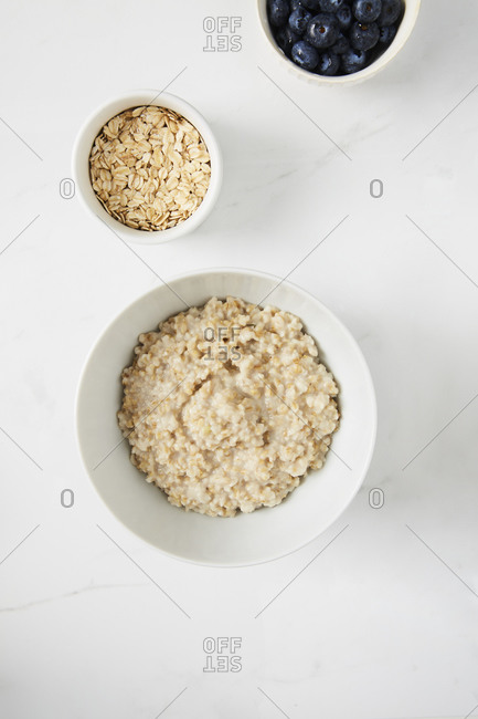 Bowl of porridge, bowl of blueberries and a bowl of oats on white marble countertop