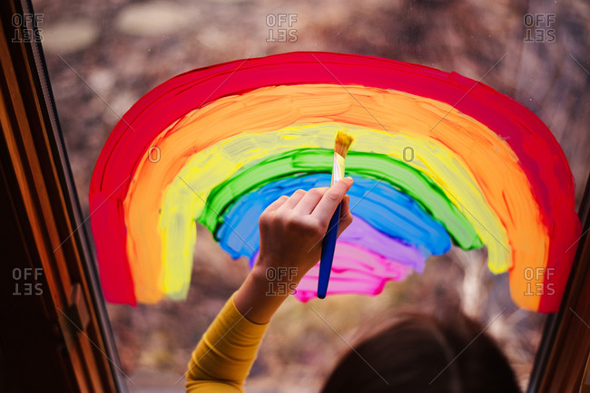 Overhead view of young girl painting rainbows on a window to support Stay-at-Home
